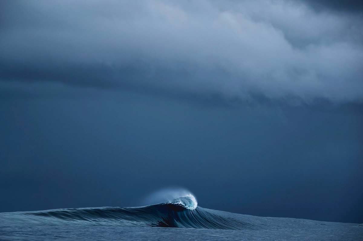 Shot at water level, this intimate view shows the undulating surface of dark ocean swells with light catching the peaks and foam creating texture across the navy blue water.