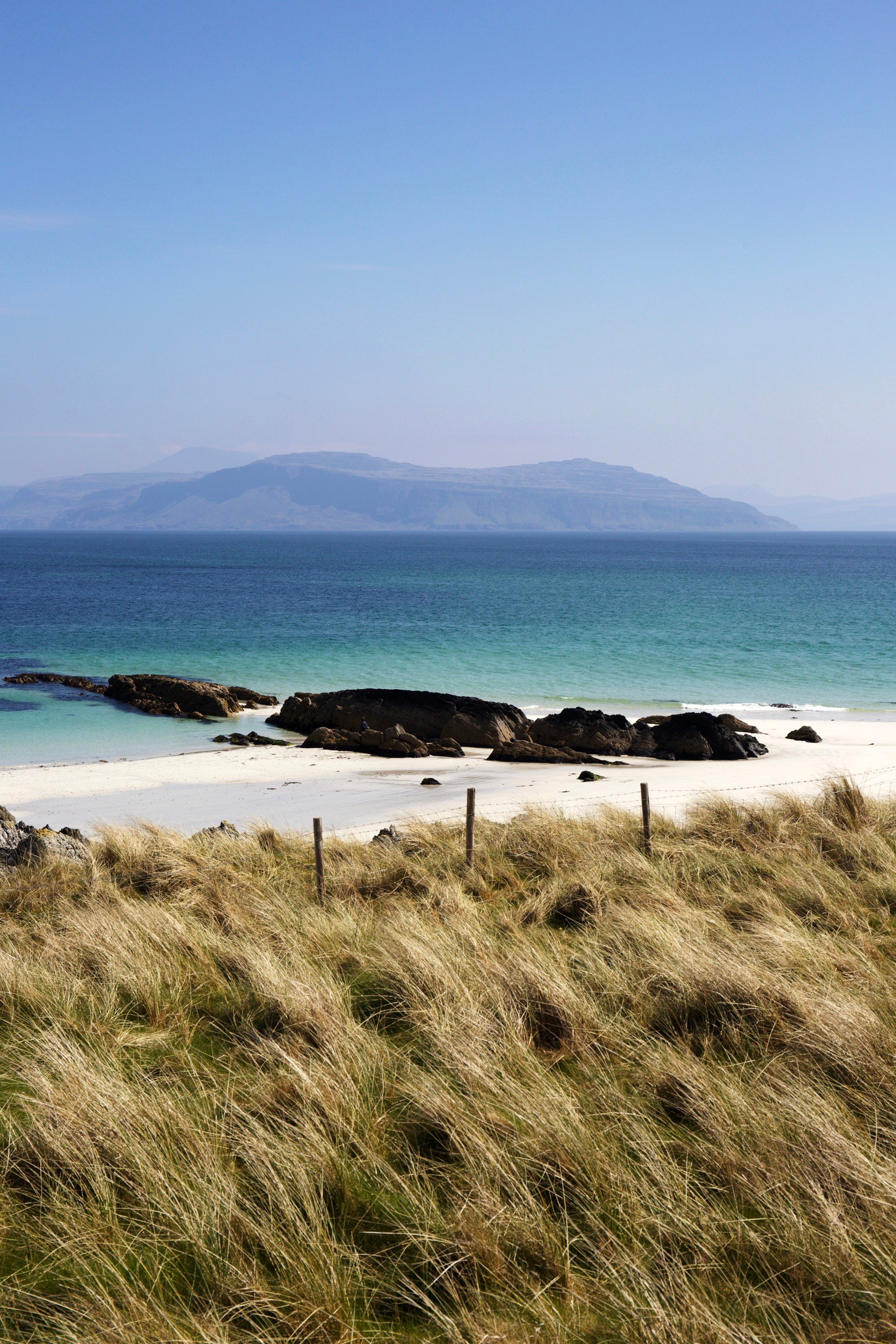 White Sand Beach With Dark Rocks Turquoise Water Grass Dunes