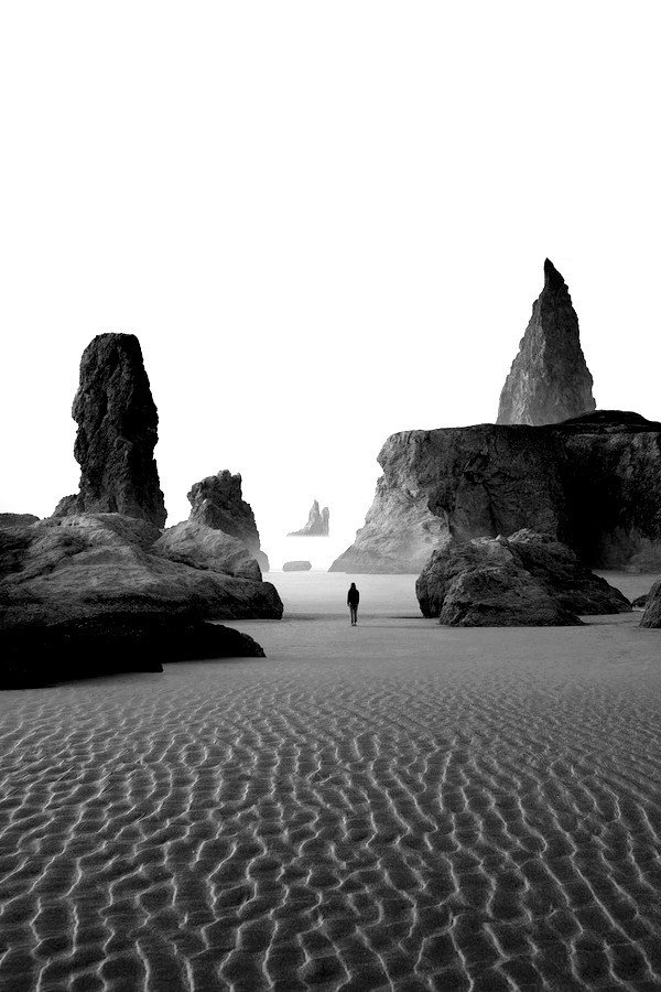Person Walking Between Black Rock Formations Sandy Beach Low Tide