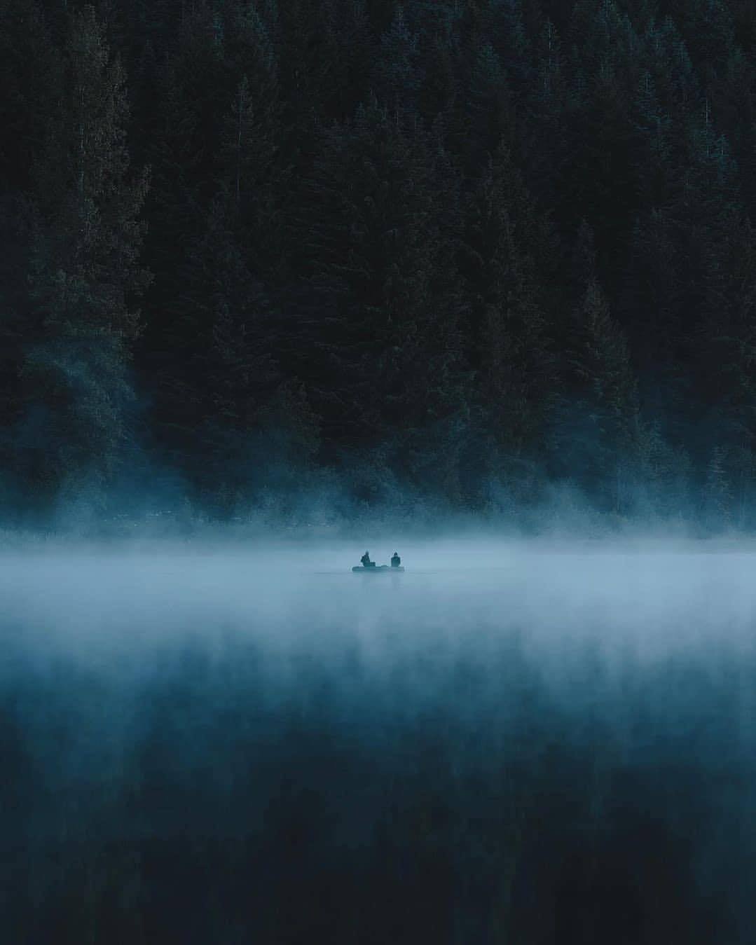 Two People Canoeing In Fog On Misty Lake With Forest