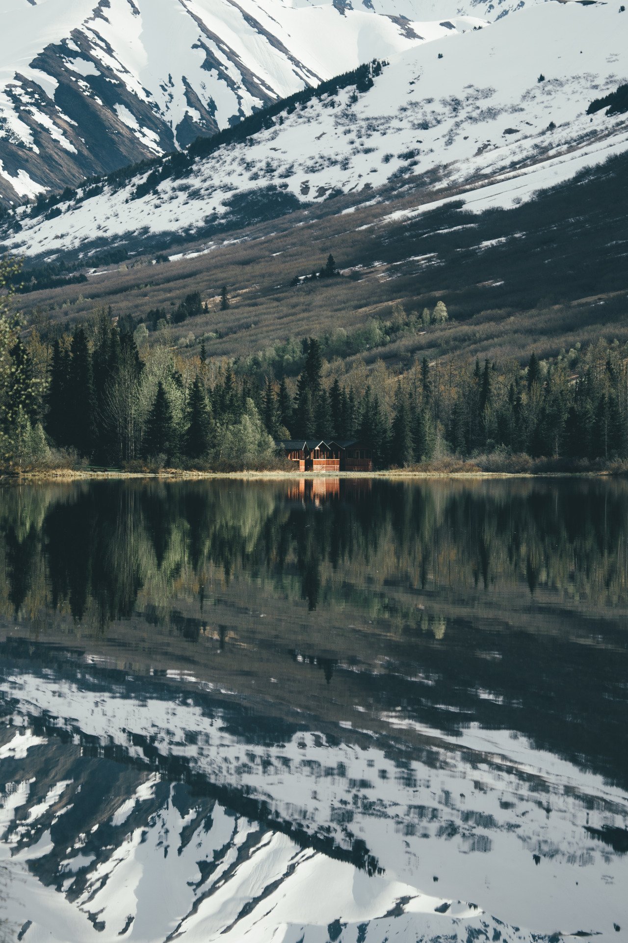 Snow Capped Mountains Reflected In Lake With Cabin Forest