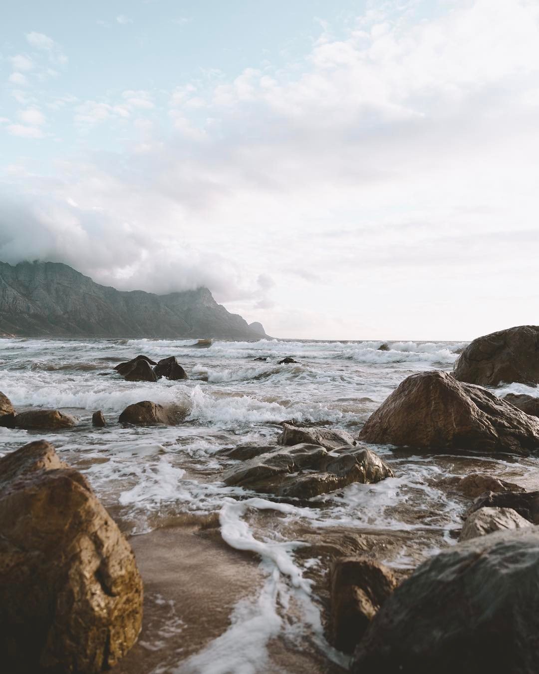 Rocky Coastline With Crashing Waves Mountain Backdrop Cloudy Sky