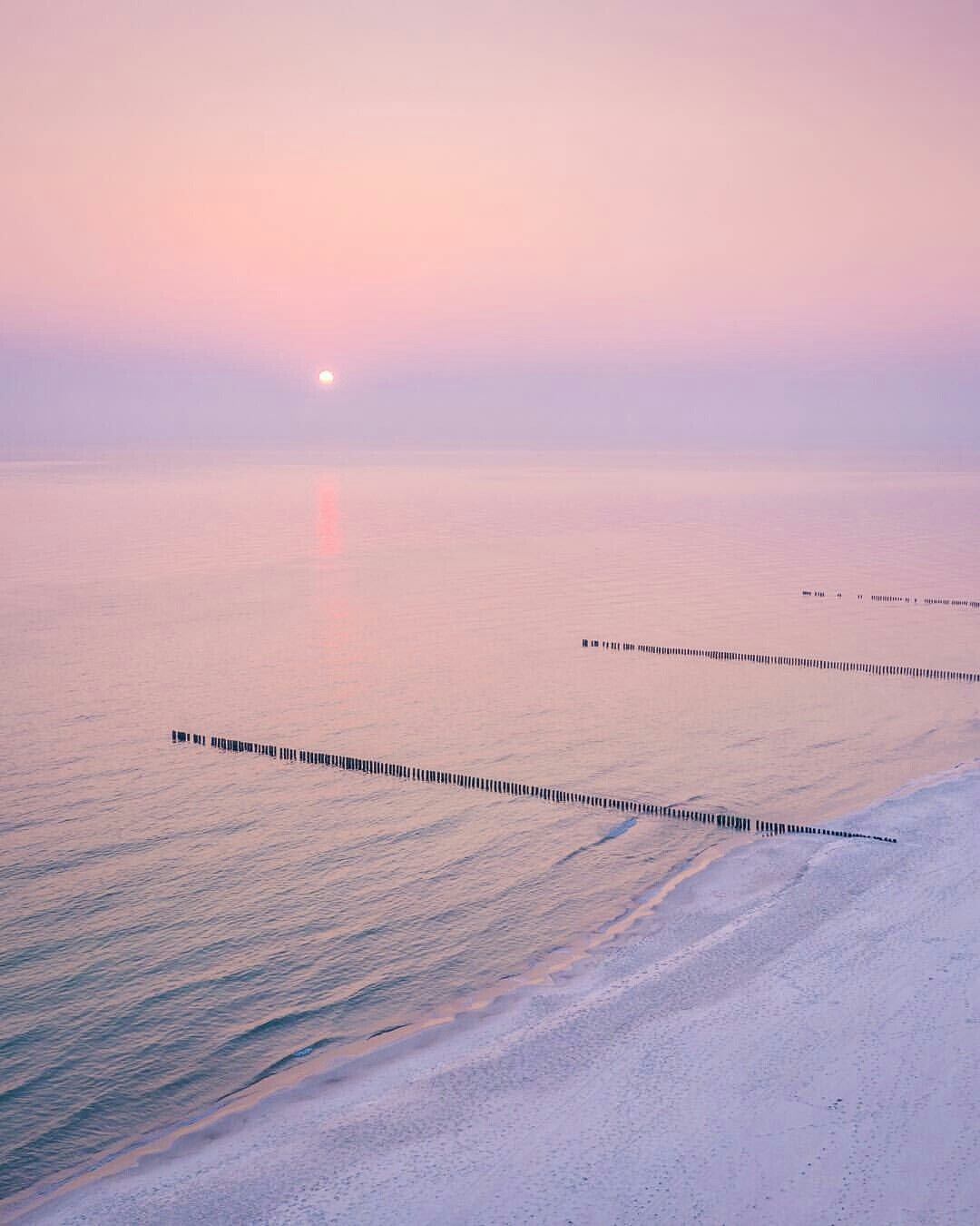 Pink Sunset Over Calm Ocean Water With Wooden Posts Beach